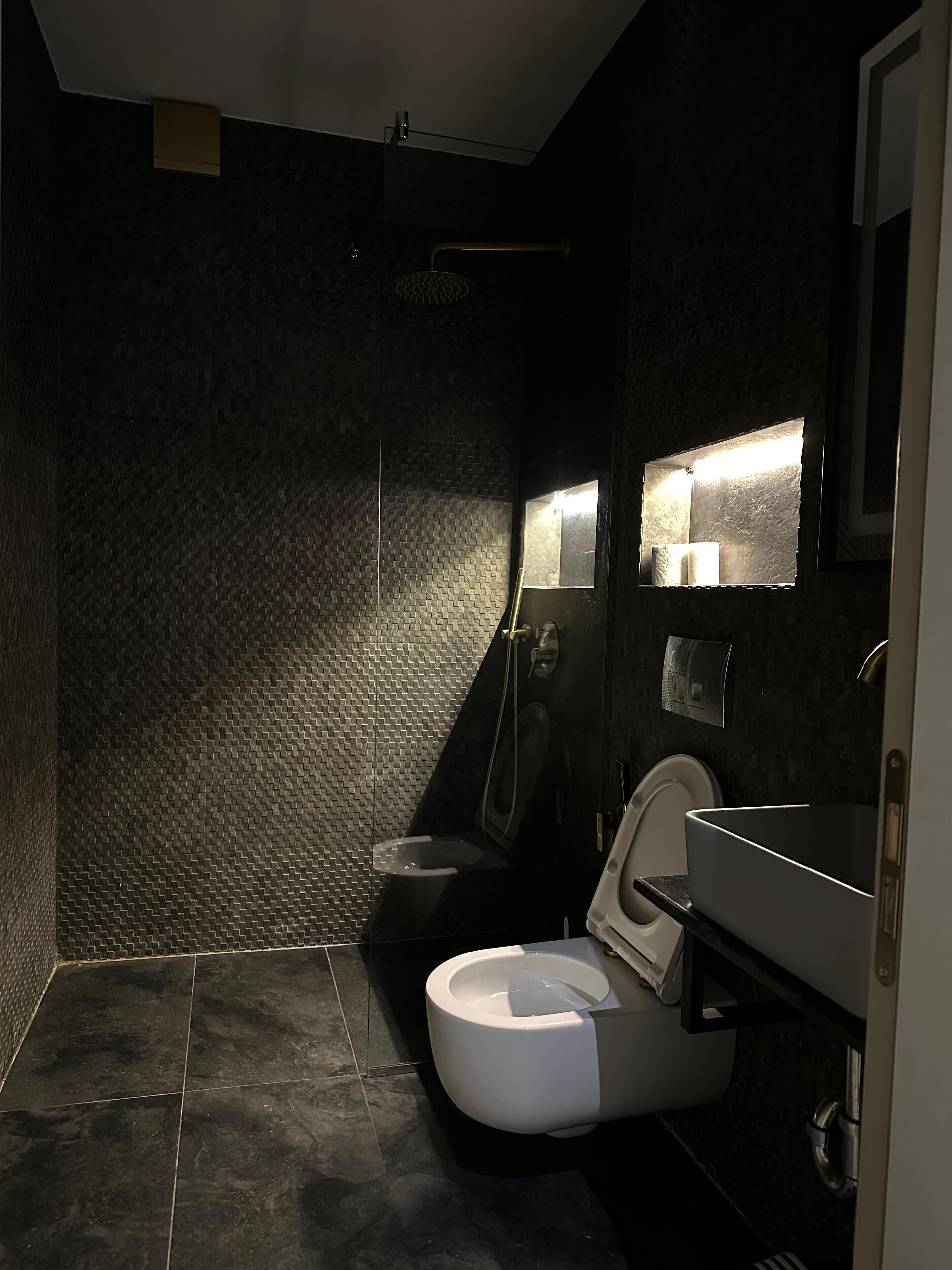A modern bathroom with a dark tiled floor, a white toilet, and a shower area.