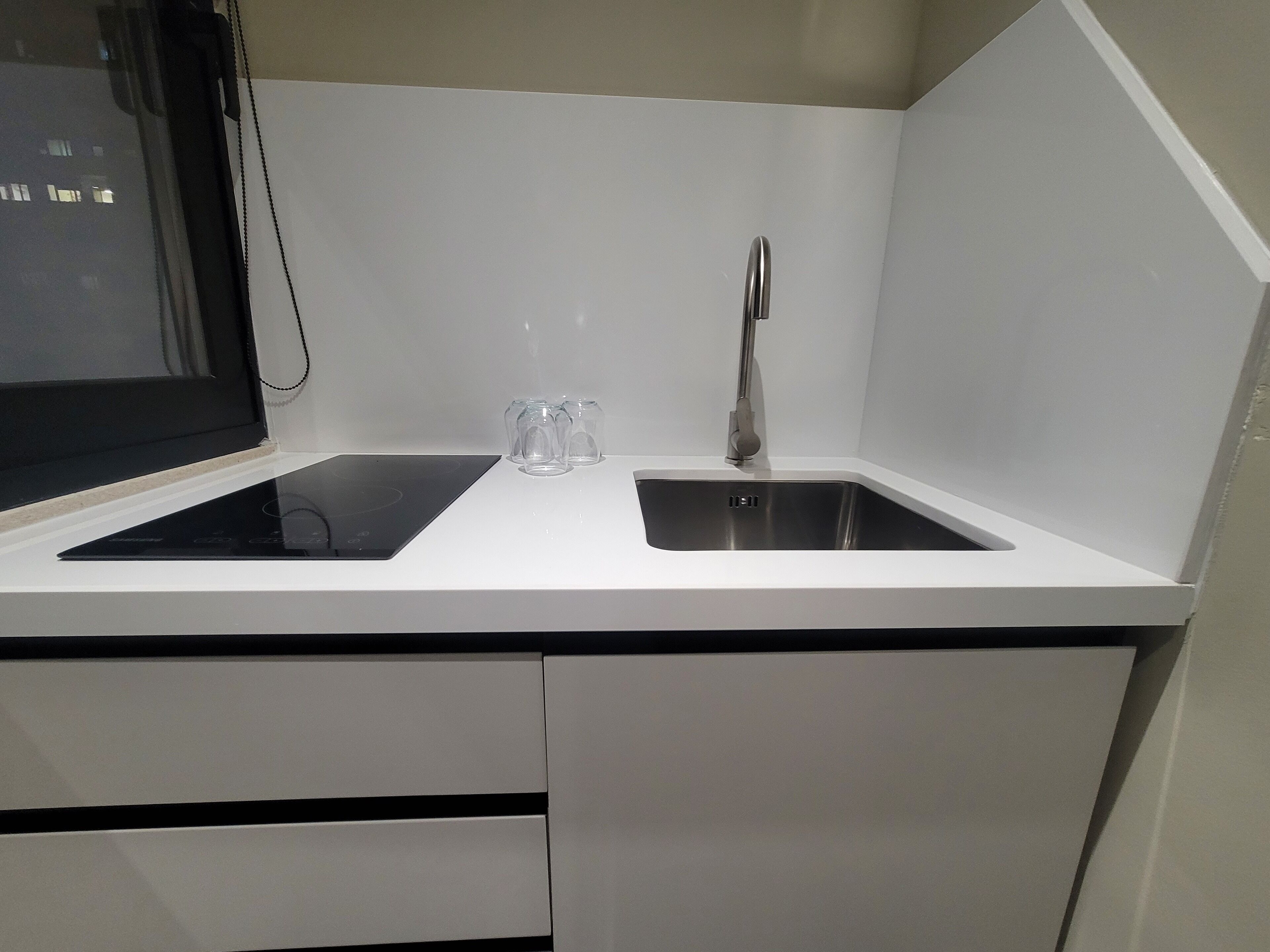Una cocina moderna con encimera blanca, dos fregaderos y un ventanal.