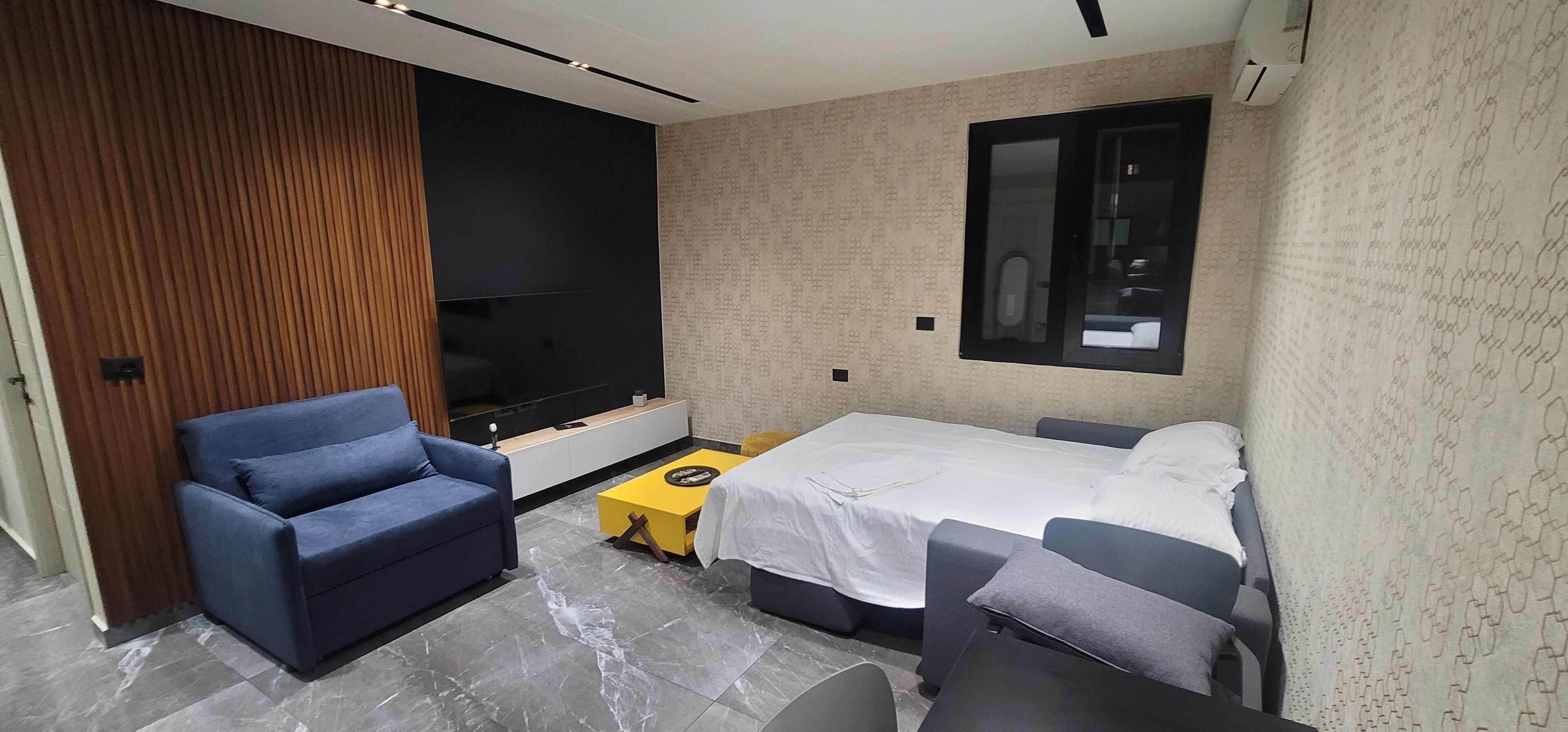 A modern hotel room with a sofa, a bed, a small table, and a TV.