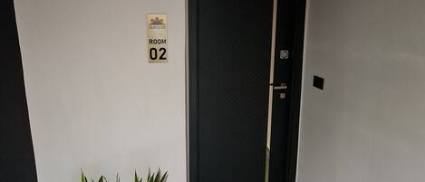 A hallway with a sign indicating Room 02, a black door, and a plant in a planter.