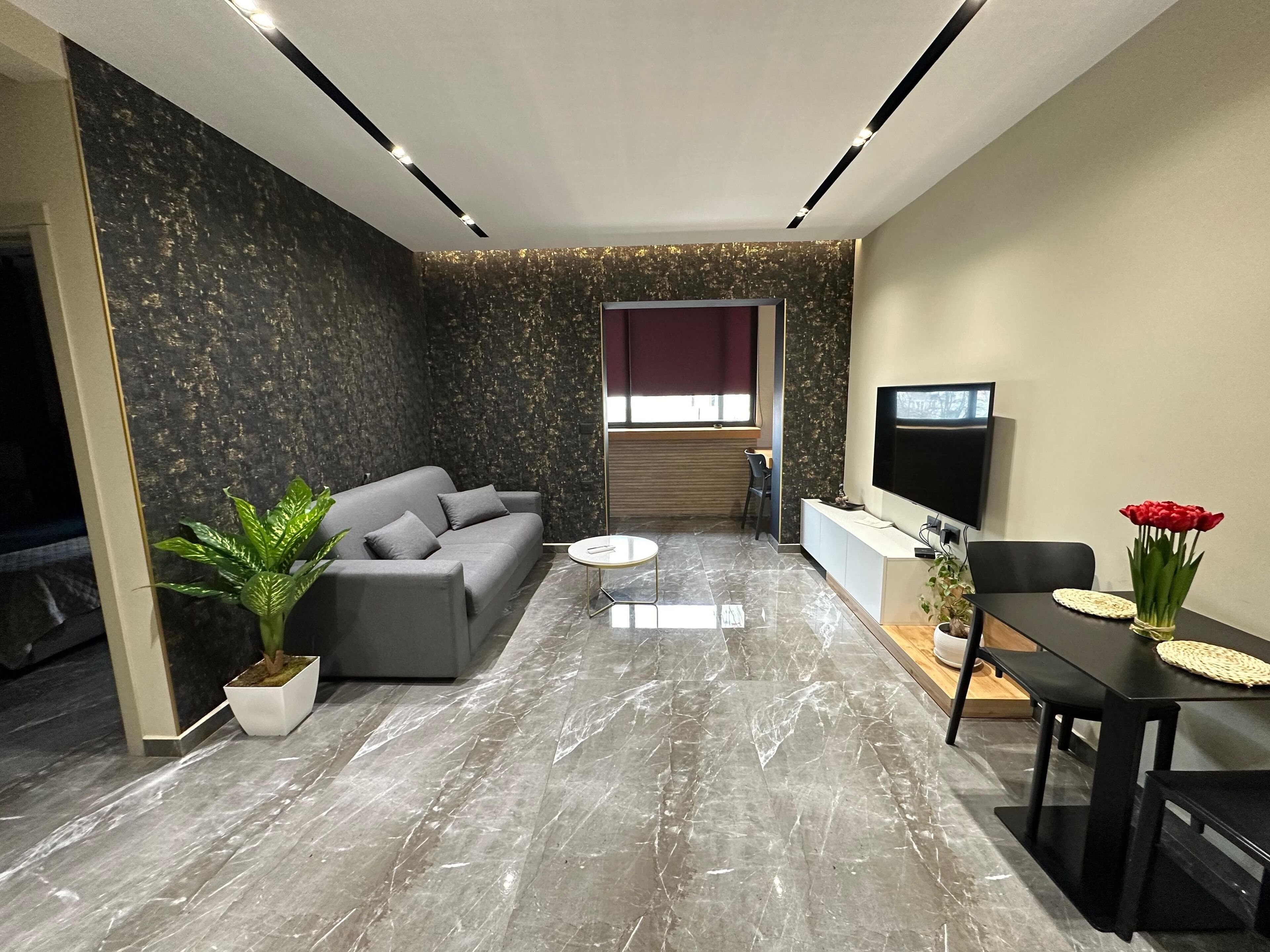 Ein modernes Wohnzimmer mit grauem Sofa, Couchtisch, Fernseher und Essbereich mit Tisch und Stühlen.