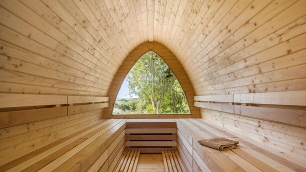 Un sauna avec des bancs en bois et une grande fenêtre en arc de cercle.