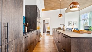 Une cuisine moderne avec des meubles de couleur bois foncé, un îlot central et des luminaires suspendus.