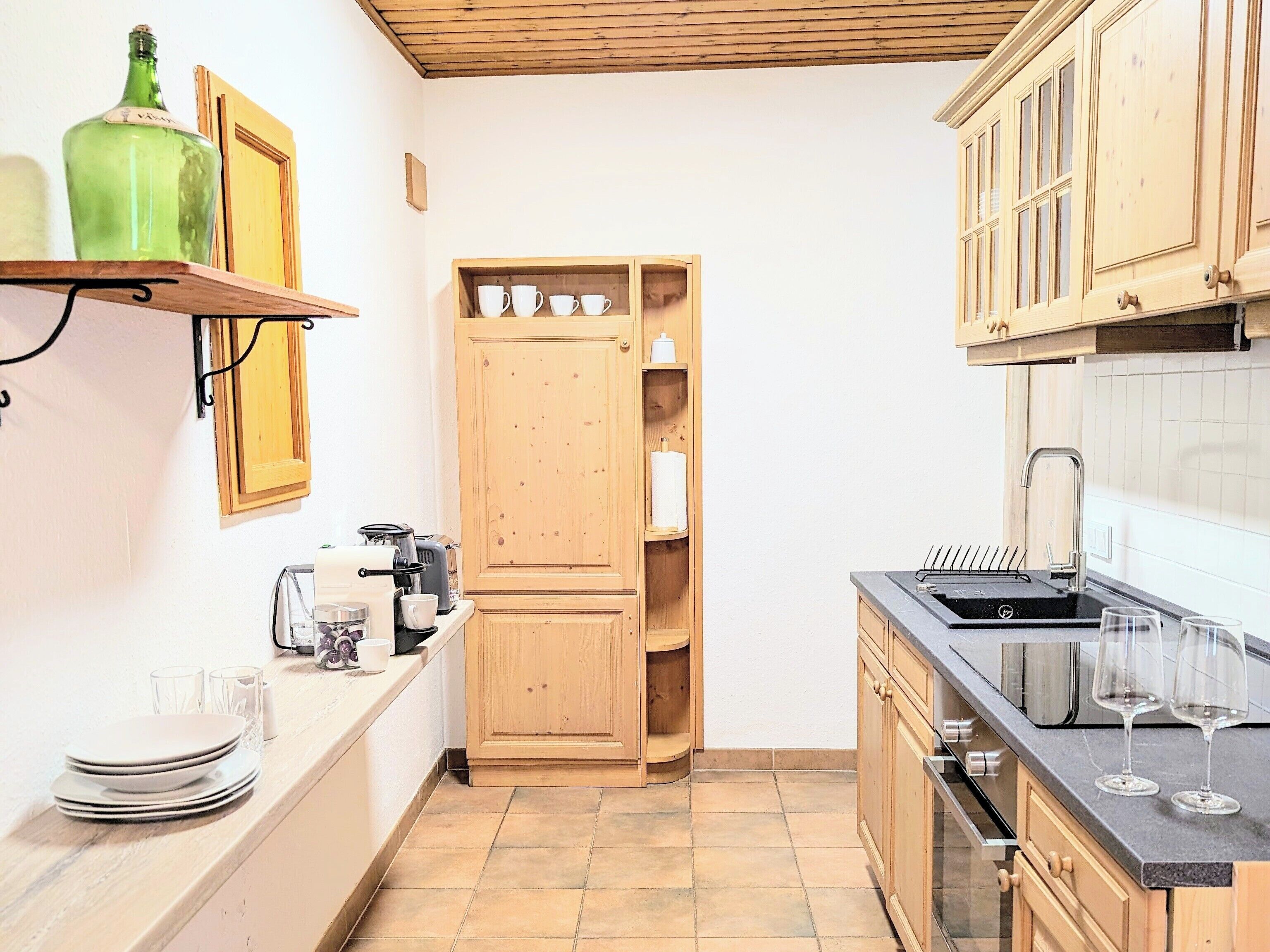 Een compacte keuken met houten kastjes, een inbouwoven, een spoelbak met afwasspartel en een klein aanrecht.