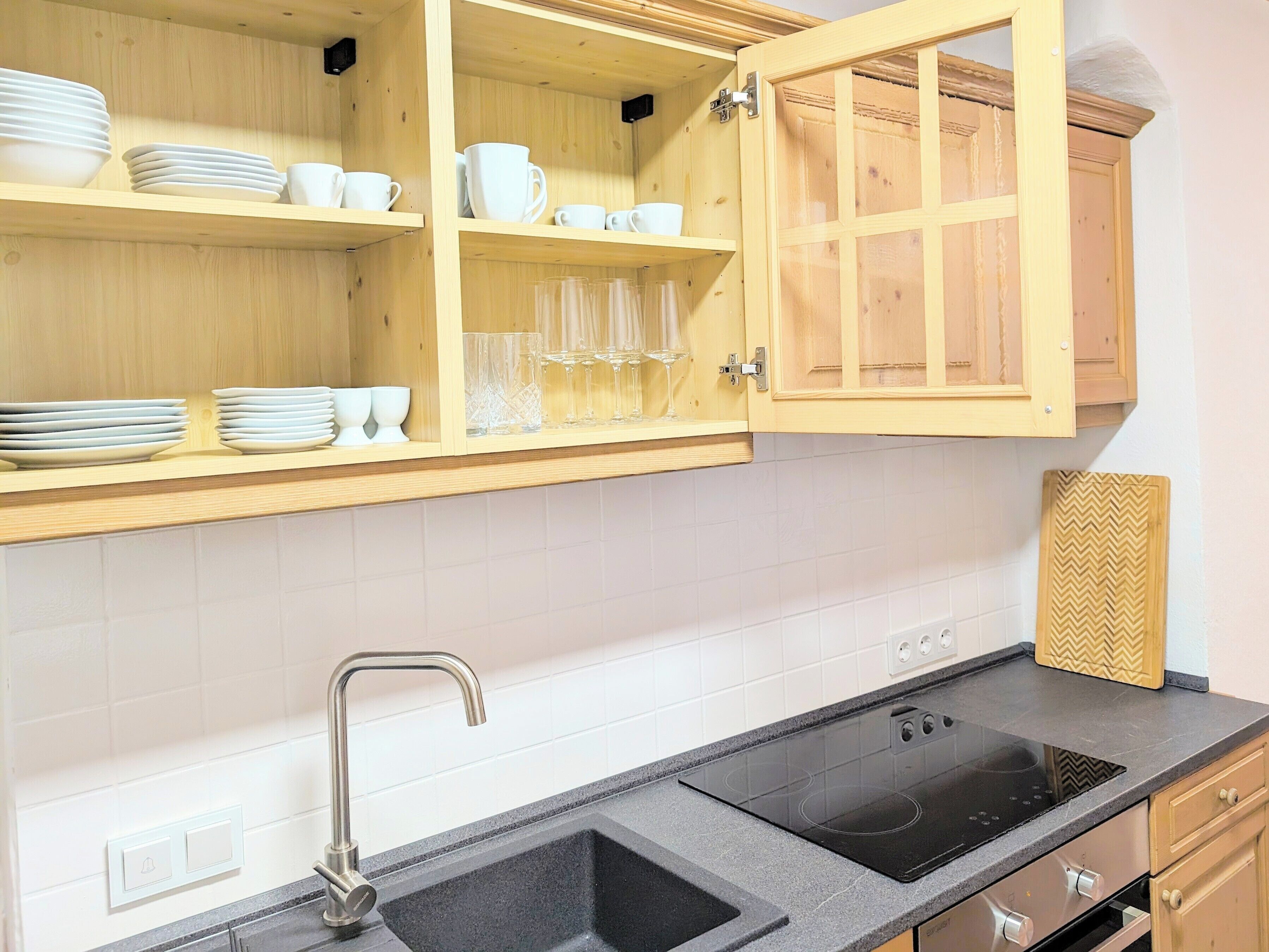 A kitchen with wooden cabinets, a black countertop, a sink, and a built-in stove.
