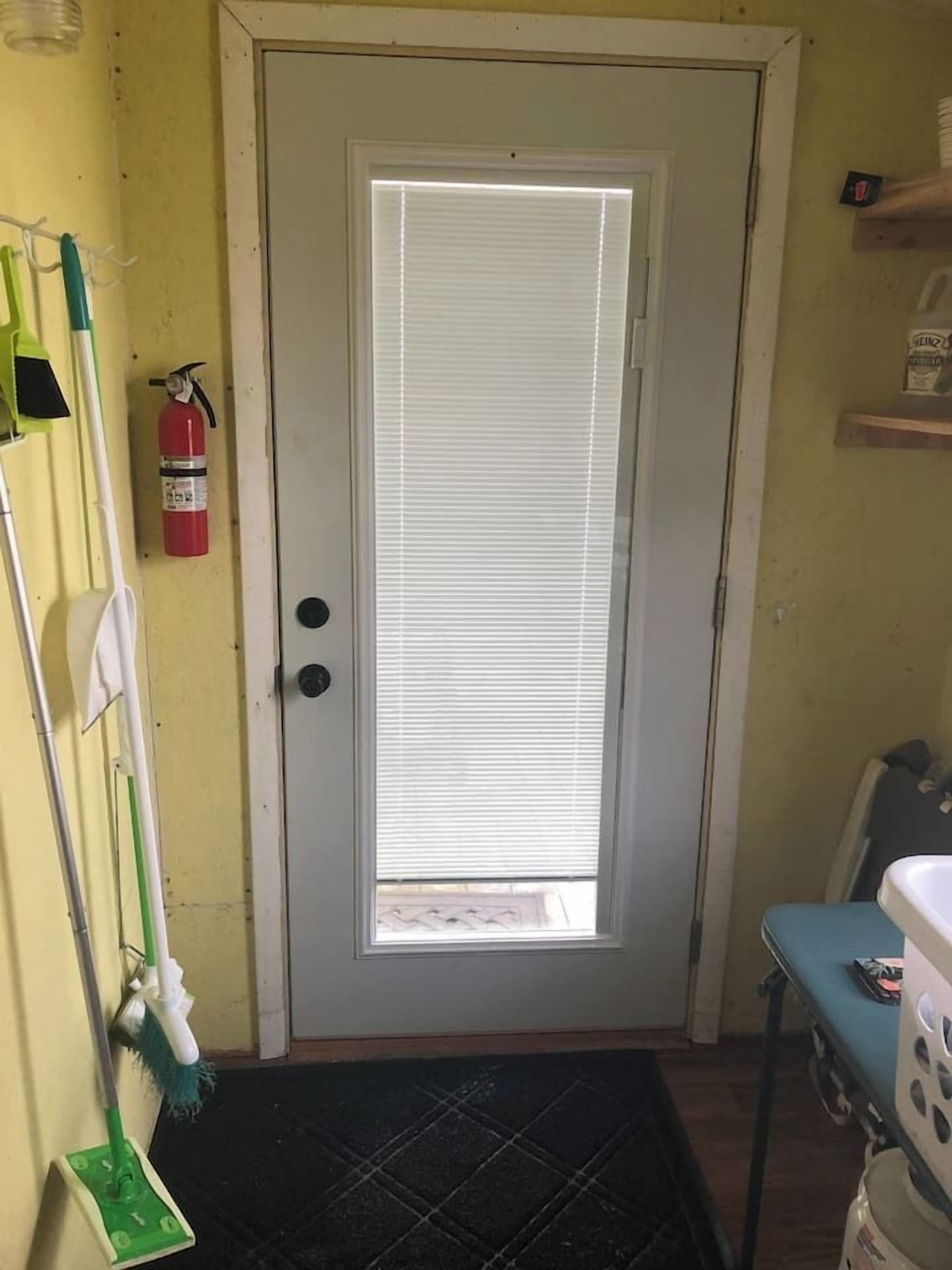 Une pièce avec une porte, un extincteur, une serpillière et une chaise.