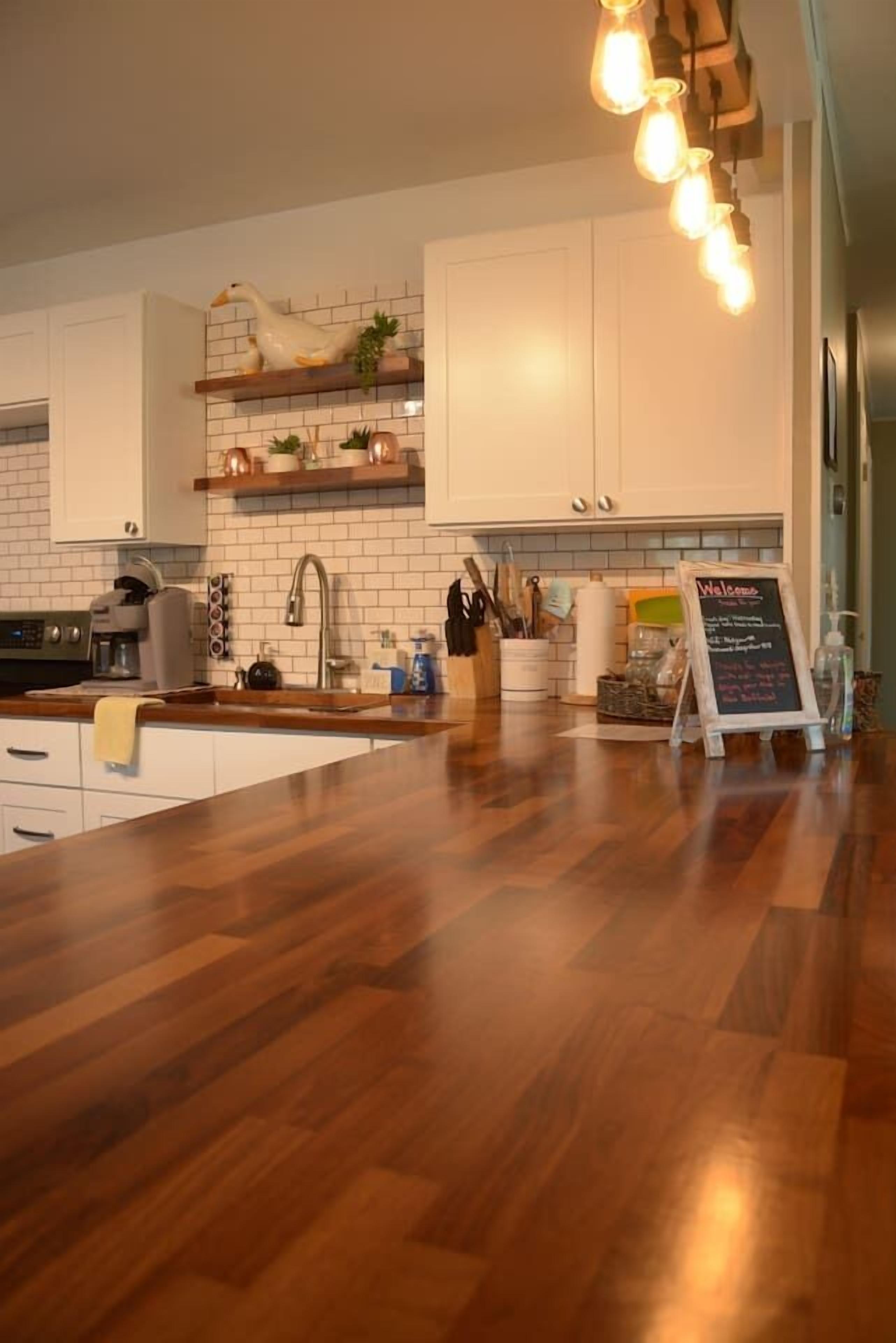 A modern kitchen with white cabinets, a wooden countertop, and a hanging light fixture.