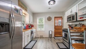 Una cocina moderna con electrodomésticos de acero inoxidable, armarios blancos y una encimera de madera.