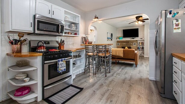 Una cocina moderna con armarios blancos, electrodomésticos de acero inoxidable y un comedor con mesa y sillas de madera.