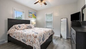 Un dormitorio con una cama, ventilador de techo, cómoda y televisor.