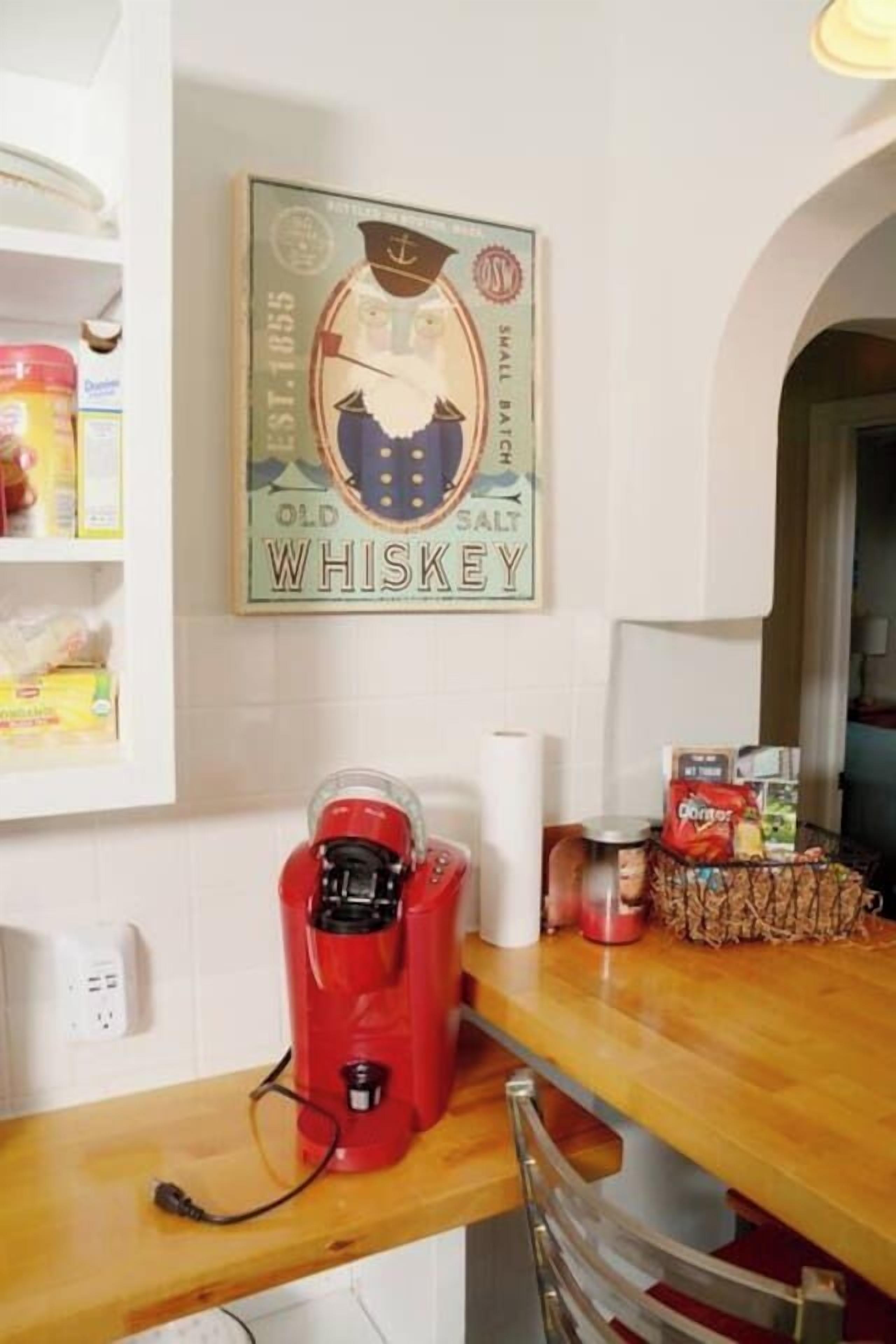 Eine Küche mit einer Kaffeemaschine auf der Arbeitsplatte, einem Regal voller Lebensmittel und einer Wanddekoration zum Thema Whiskey.