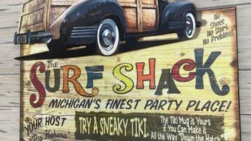 En träskylt med en illustration av en klassisk bil och text som marknadsför ”The Surf Shack” som Michigans bästa festplats, där man kan få mat, dryck och en tiki-mugg.