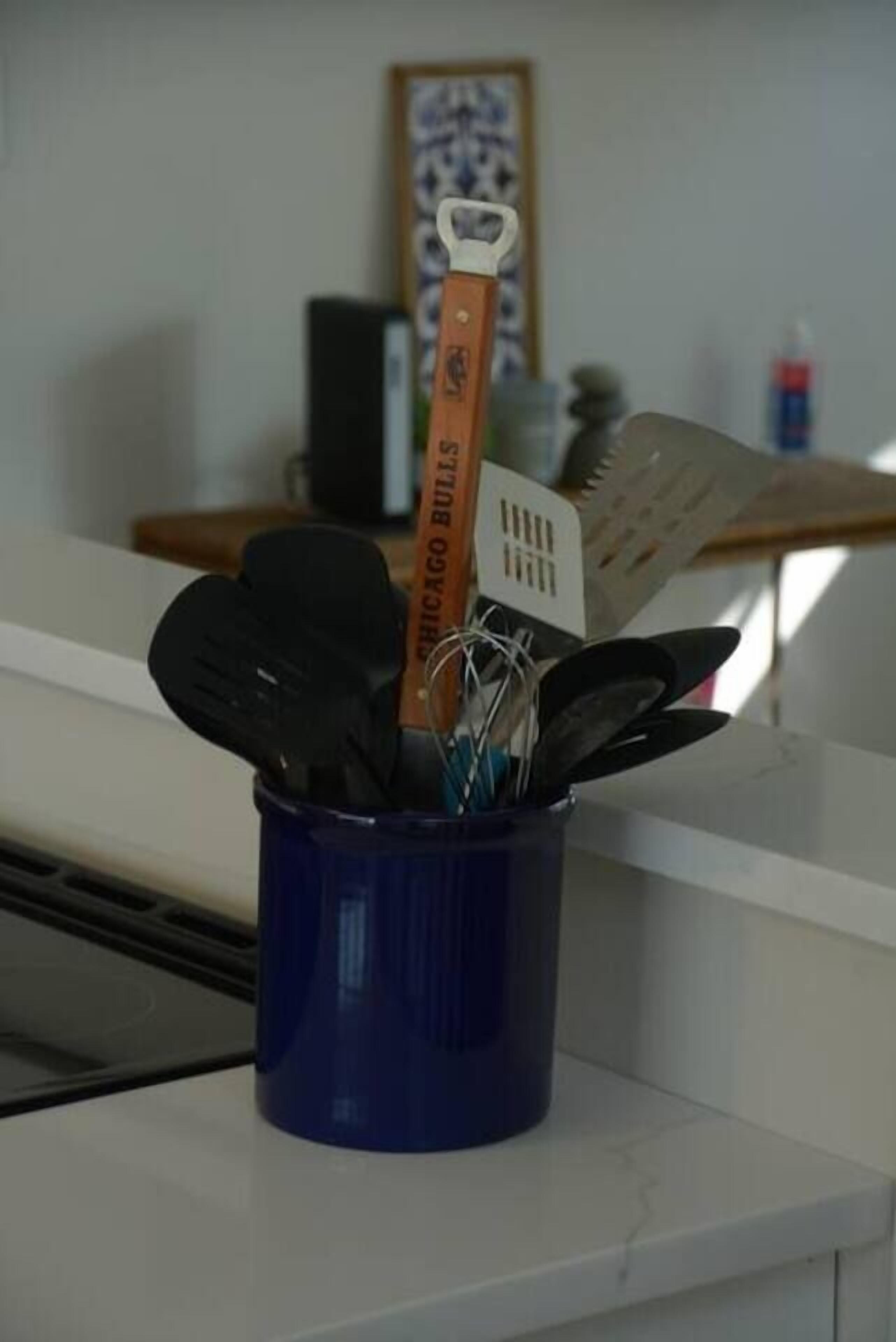 Een keukentrap met een blauwe keukengerei-houder met een spatel en ander keukengereedschap.