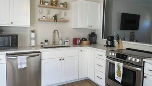 A modern kitchen with white cabinets, a stainless steel dishwasher, a double oven, and a flat-screen TV mounted above the oven.