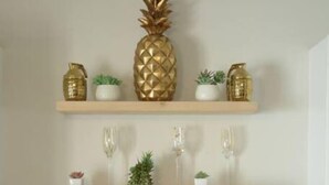 A kitchen with a stainless steel sink, wooden shelves with decorative items, and a gold faucet.