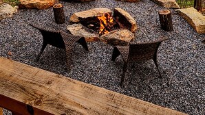 Ein Lagerfeuer, umgeben von Steinen und Kies, mit einem Holzboden im Vordergrund.