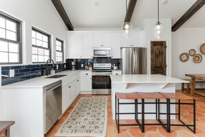 A modern kitchen with white cabinets, a stainless steel refrigerator, a built-in oven, and a large island with a bench. - Owner's Suite - 3 Bedroom Casita (Nemo)