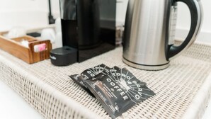 A coffee maker, a kettle, and coffee pods on a woven tray.
