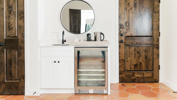 A kitchen with white cabinets, a stainless steel refrigerator, a coffee maker, and a wooden door.