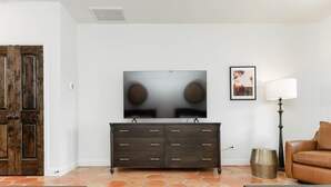 A living room with a dark wooden cabinet, a brown leather sofa, a patterned rug, and a wall-mounted TV. - 3 Bedroom Casita (6 Queen Beds) (Nemo)