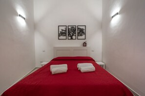 Une chambre d’hôtel avec une couvre-lit rouge, deux serviettes blanches, une tête de lit blanche et trois tableaux encadrés accrochés au mur.
