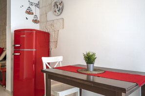 Une cuisine de taille modeste, avec un réfrigérateur rouge, une chaise blanche, une table à manger avec un set de table rouge et une petite plante en pot posée sur la table.