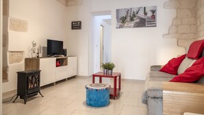 Un salon comprenant un téléviseur, un canapé, un pouf et une petite table sur laquelle est posée une plante.