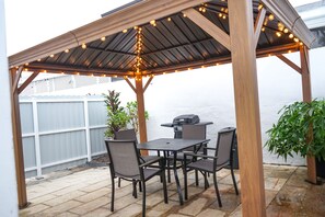 Ein überdachter Patio-Bereich mit Grill und Sitzgelegenheit.