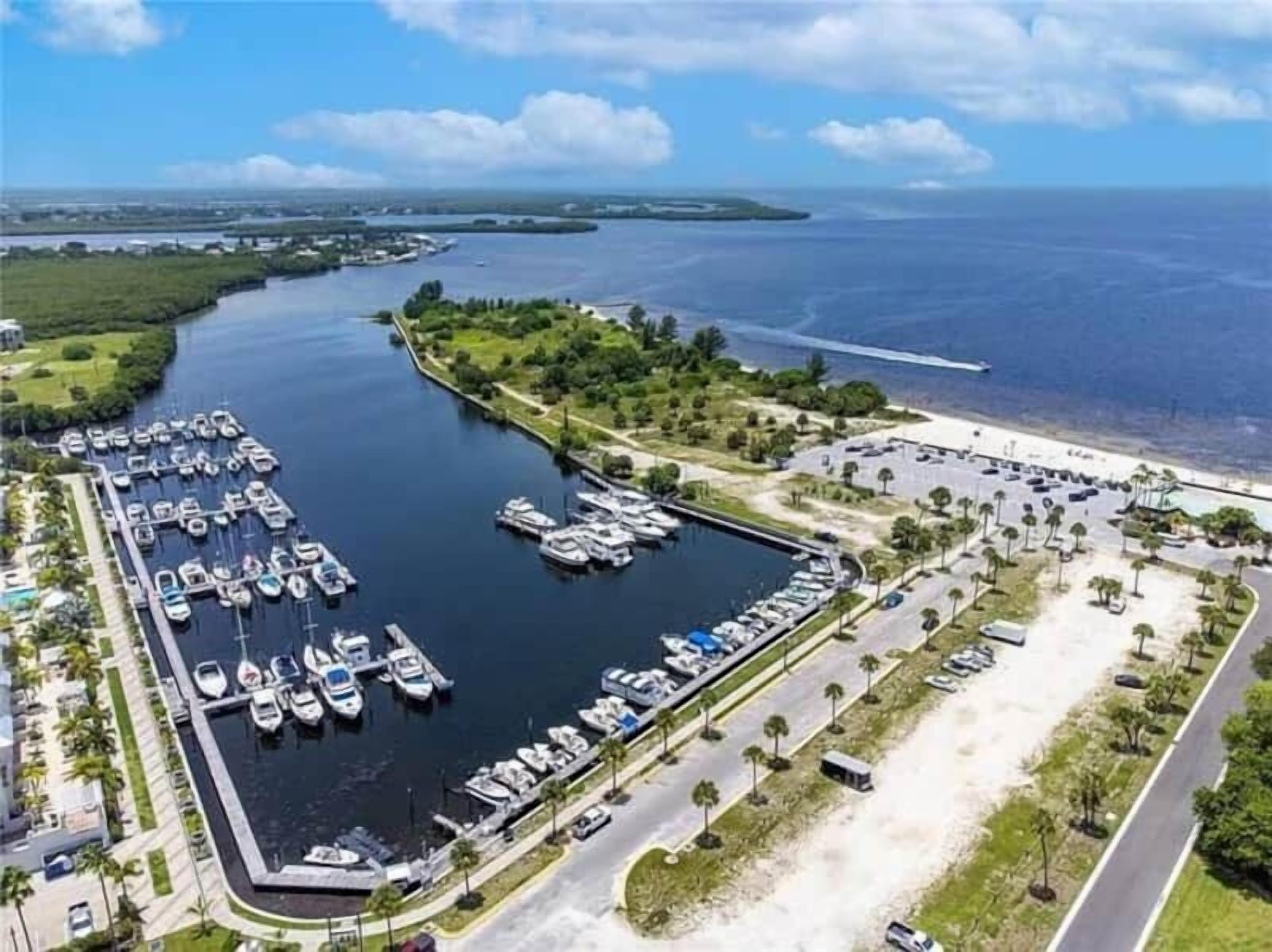Een luchtendicht uitzicht op een jachthaven met veel boten die aanmeren, een parkeerplaats en een strand op de achtergrond.