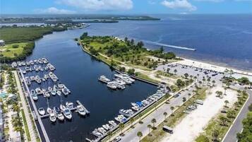 An aerial view of a marina with numerous boats docked, a parking area, and a beach in the background.
