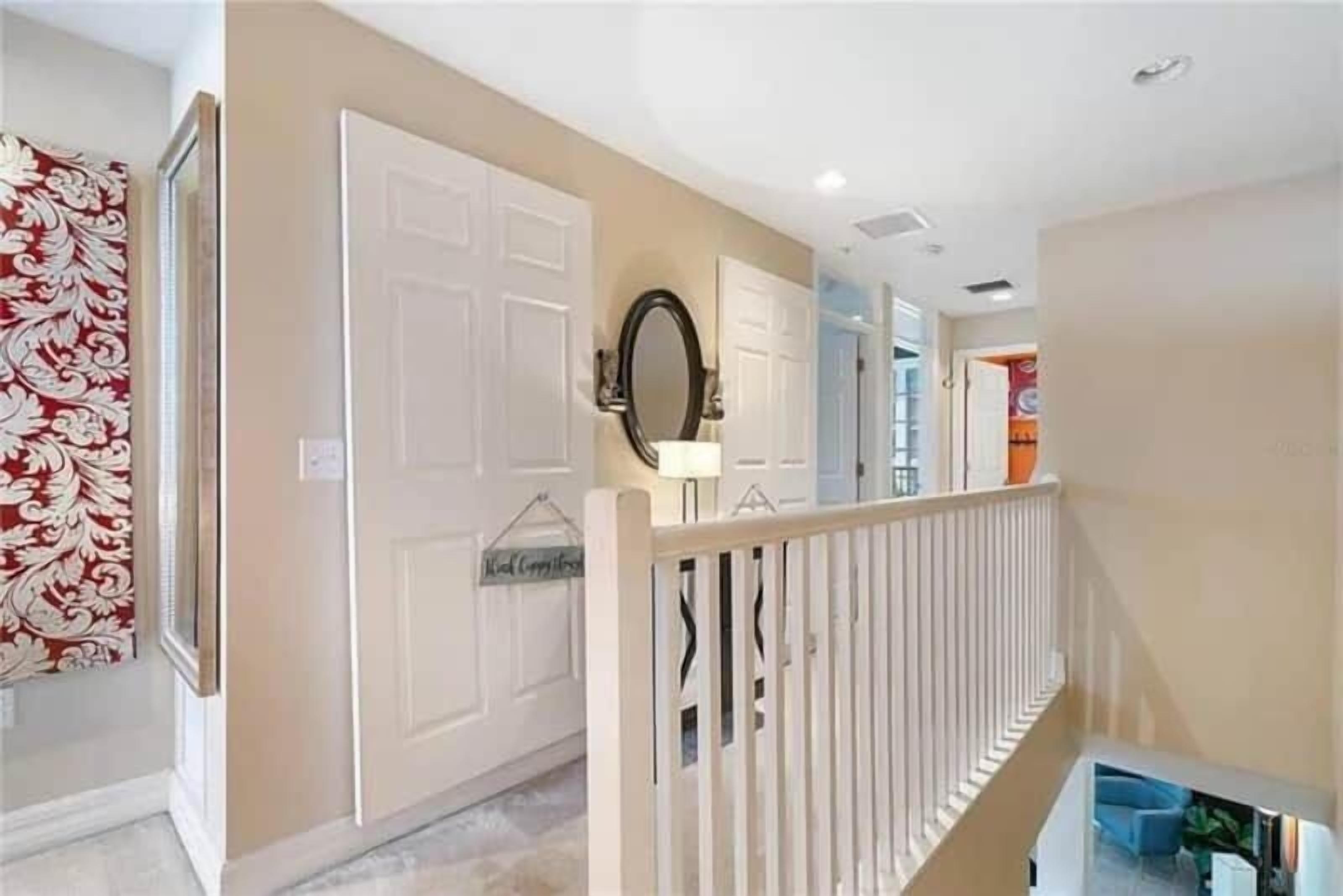 A hallway with a white door, a mirror, and a decorative wall hanging.
