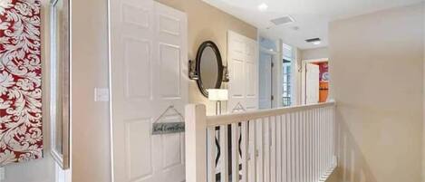 A hallway with a white door, a mirror, and a decorative wall hanging.