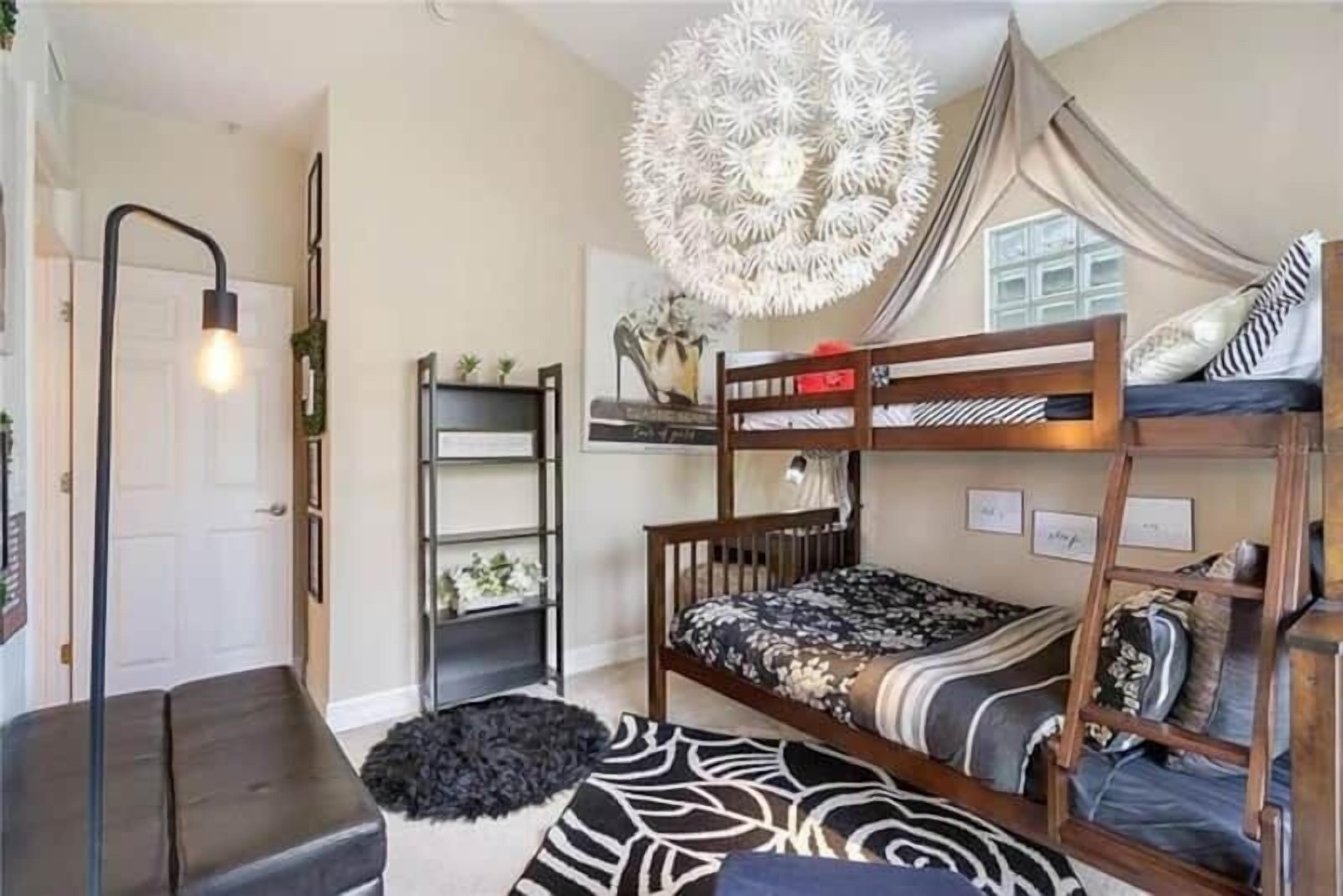 A compact room with a bunk bed, a desk, a chair, and a decorative light fixture.