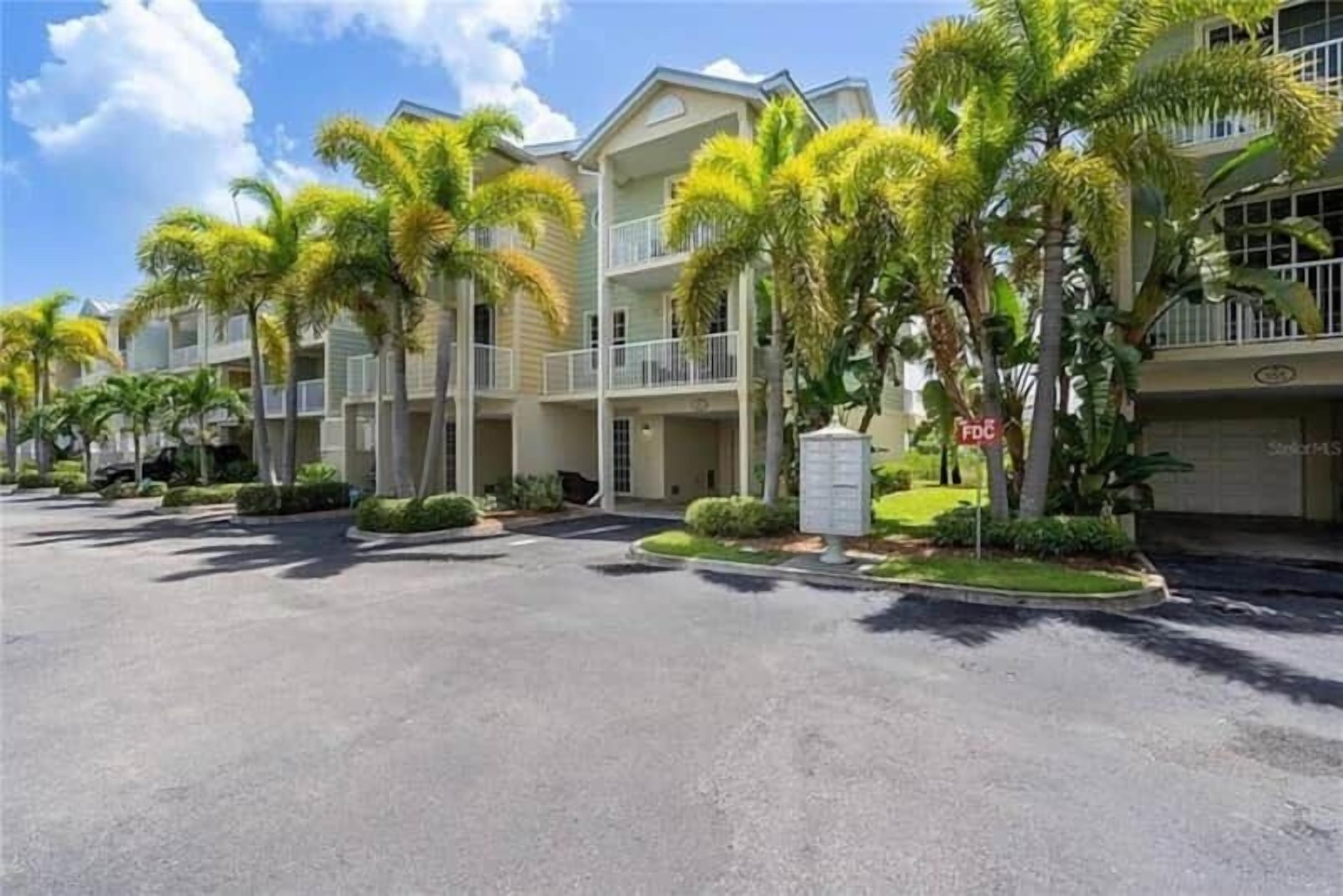 A row of two-story buildings with balconies, surrounded by palm trees and a clear sky.