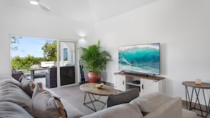 Uma sala de estar moderna com uma televisão de tela grande, um sofá confortável, uma mesa de centro e um vaso com planta.