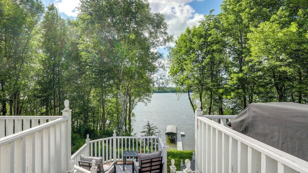 A deck with a view of a lake, surrounded by trees, and a covered grill. - Lakefront Minnesota Vacation Rental w/ Dock (Annandale)