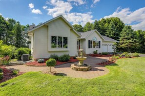Une maison à deux étages, avec un chemin en briques menant à la porte d’entrée, entourée d’un jardin bien entretenu et agrémentée d’une petite fontaine.