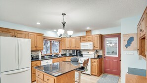 A kitchen with wooden cabinets, a white refrigerator, a microwave, and a bar stool. - Lakefront Minnesota Vacation Rental w/ Dock (Annandale)