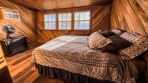 Un dormitorio rústico de cabaña con una cama, un ventilador y una ventana.