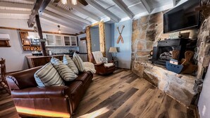 Una sala de estar acogedora con chimenea de piedra, sofá de cuero y piso de madera.