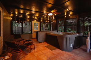 Un espace avec un jacuzzi, doté d’un ventilateur de plafond, de guirlandes lumineuses et de chaises longues en bois.