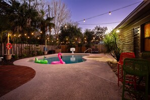 Um quintal com piscina, boia de flamingo e luzes de cordão.