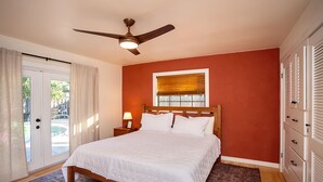 A bedroom with a bed, a ceiling fan, a window with blinds, a nightstand with a lamp, and a view of the outdoors. - New! Saltwater pool home with hot tub, game room, and outdoor games! (Gainesville)