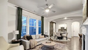 A spacious living room with a sofa, coffee table, and a dining area with chairs and a table. - Birkdale Plaza Shop-Eat-Work-Play (Huntersville)