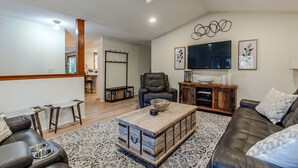 A living room with a leather sofa, a coffee table, a TV, and a ceiling fan. - Cheerful, Comfortable and Convenient 3 Bedroom Home (Eugene)
