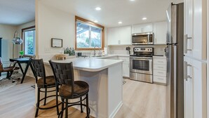 A modern kitchen with white cabinets, stainless steel appliances, and a large island with bar stools. - Cheerful, Comfortable and Convenient 3 Bedroom Home (Eugene)