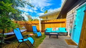 Un patio trasero con cerca de madera, una silla azul, un sofá con cojines coloridos y una hamaca.