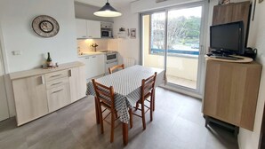 Una cocina compacta con una mesa de comedor, sillas de madera, un reloj y un televisor sobre un mueble.