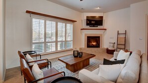 A living room with a fireplace, a ceiling fan, and a large window with blinds. - Sedona Retreat W/ Tesla Mobile Charger (Sedona)