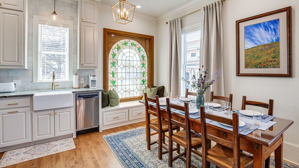 A kitchen with white cabinets, a built-in dishwasher, and a dining area with a wooden table and chairs.